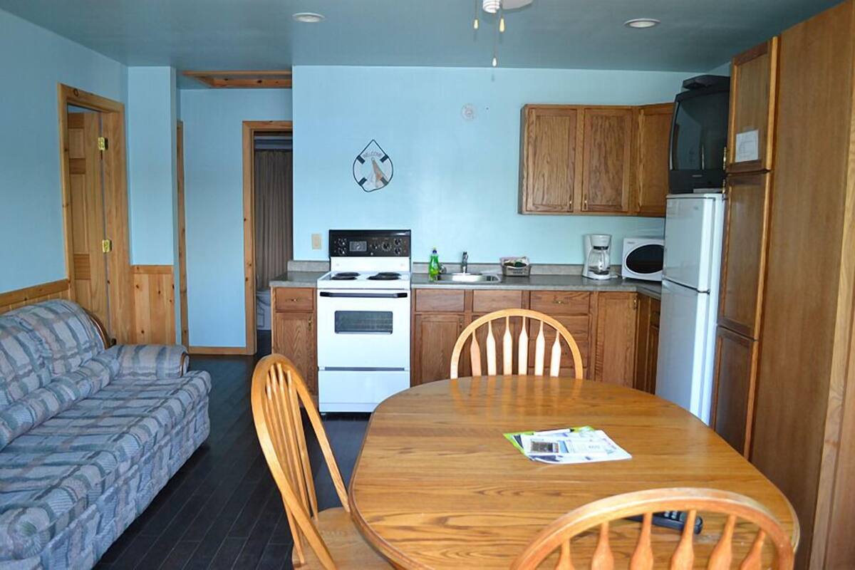 A compact kitchen with wooden cabinets, a stove, microwave, and a dining table with chairs.