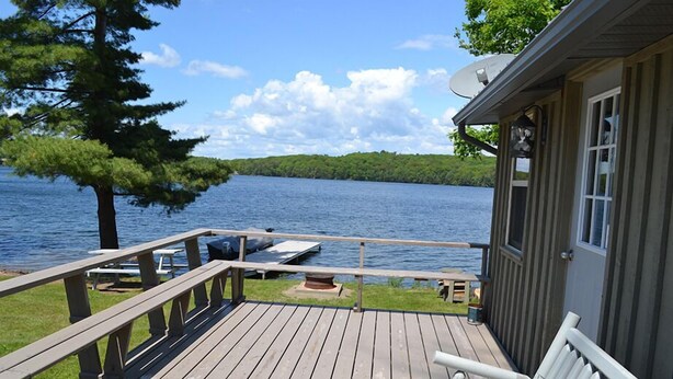 Une terrasse en bois avec un banc, donnant sur un lac où se trouvent un quai et un arbre.