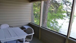Un espace extérieur abrité, doté d’une table et de chaises, offrant une vue sur les arbres et l’eau, et doté d’un plancher en bois.
