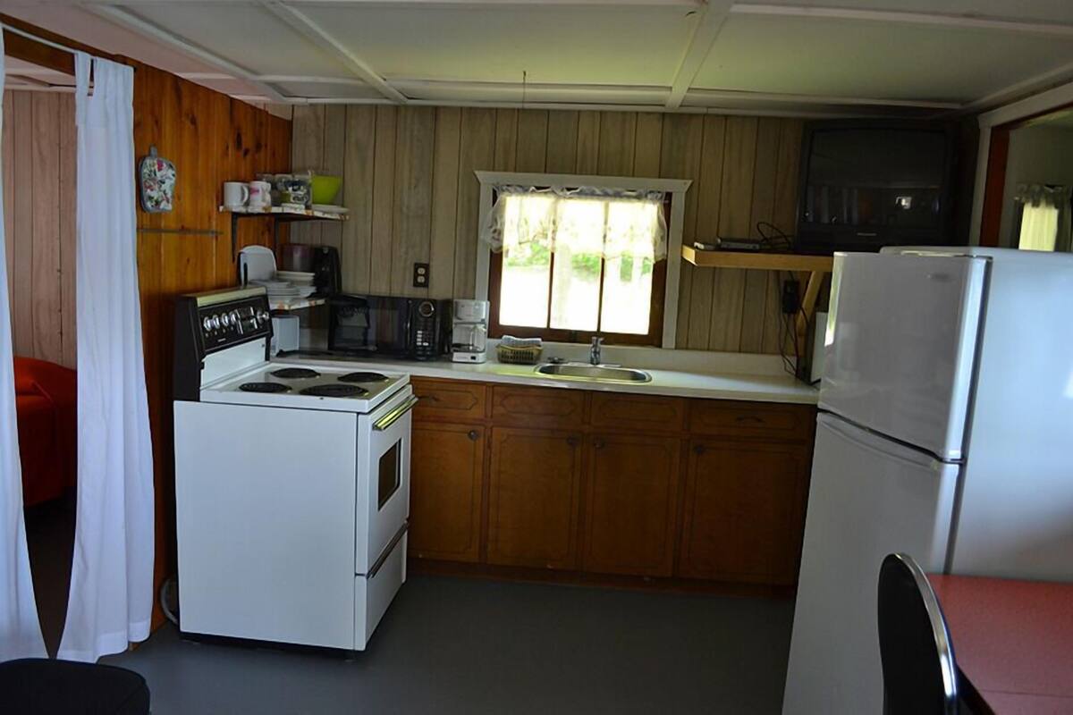 A compact kitchen with wooden cabinets, a white stove, a sink, and a refrigerator.
