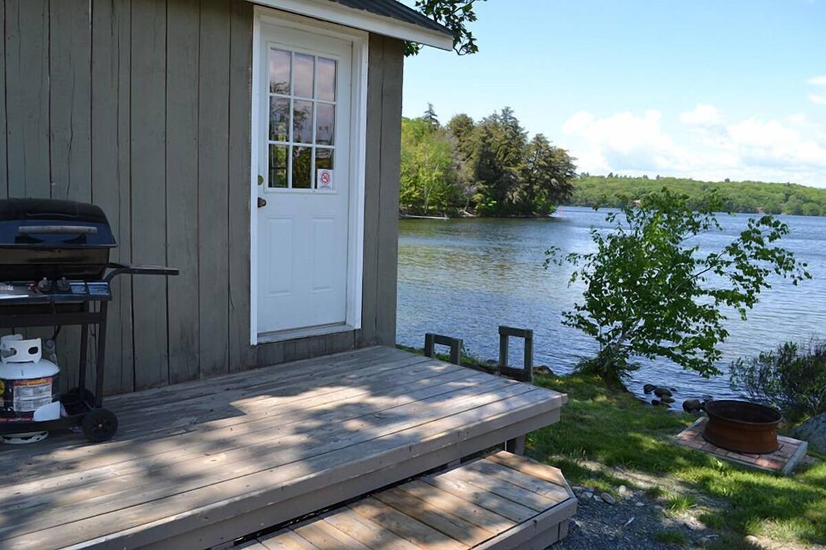 A wooden cabin with a dock extending into a lake, a grill, and a fire pit on the deck.