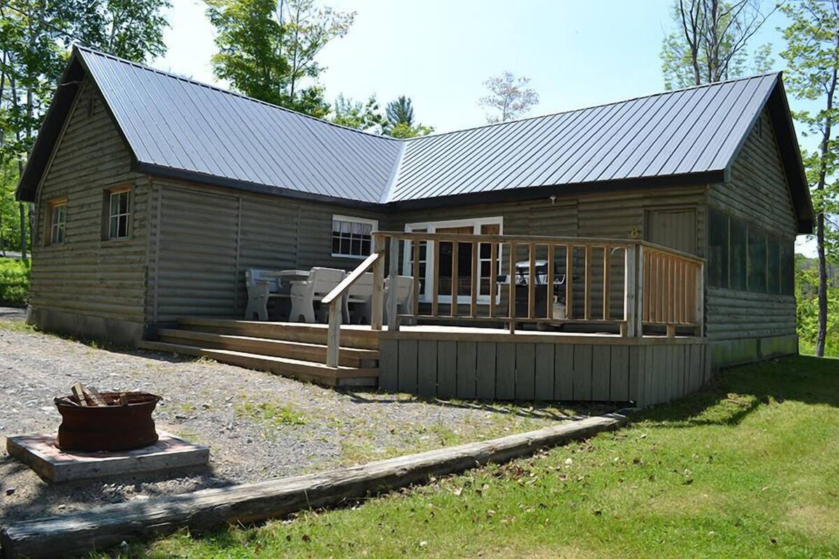 A log cabin with a metal roof, a porch with wooden railings, and a fire pit in front.