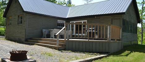 A log cabin with a metal roof, a porch with wooden railings, and a fire pit in front.