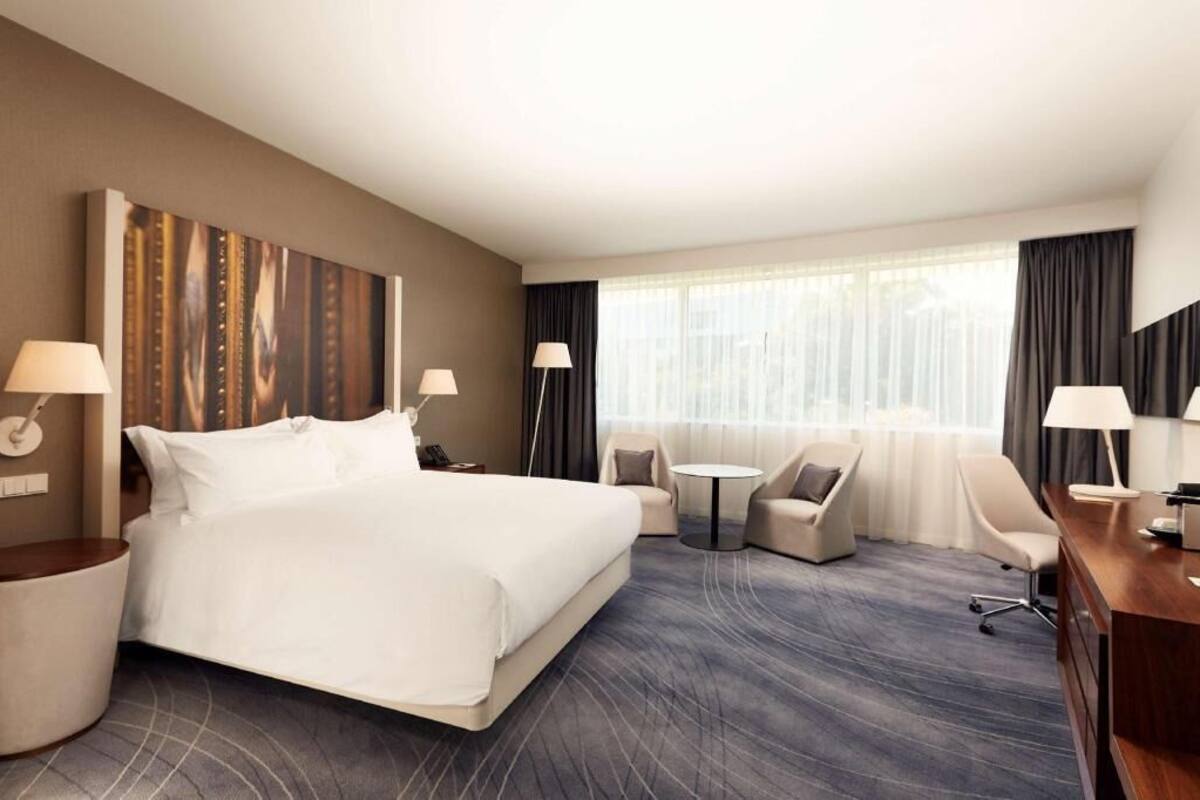Una habitación de hotel con una cama grande, dos sillones, un escritorio y una pequeña mesa redonda.