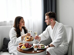 A couple in white bathrobes sitting at a round table with breakfast items and glasses of white wine. - DoubleTree by Hilton Hotel Wroclaw (Wroclaw)