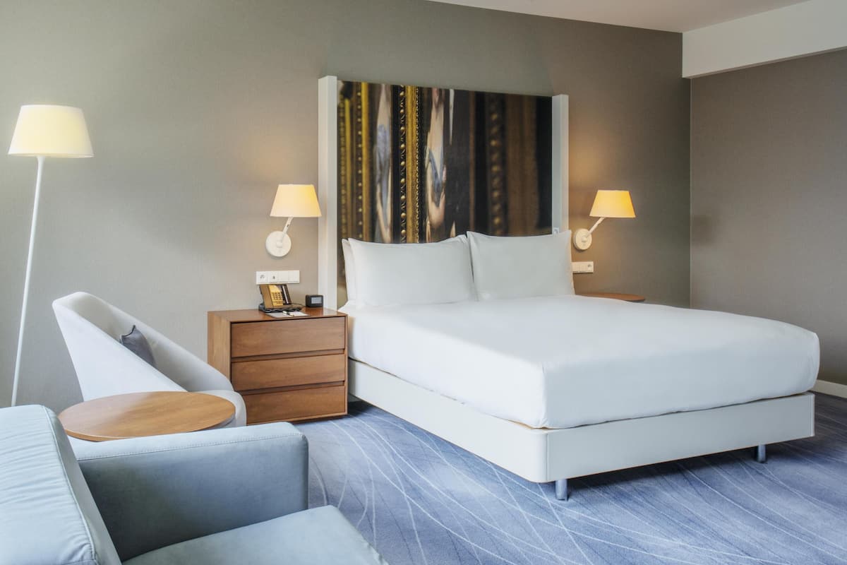 Una habitación de hotel moderna con cama, mesitas de noche, una silla y una lámpara.