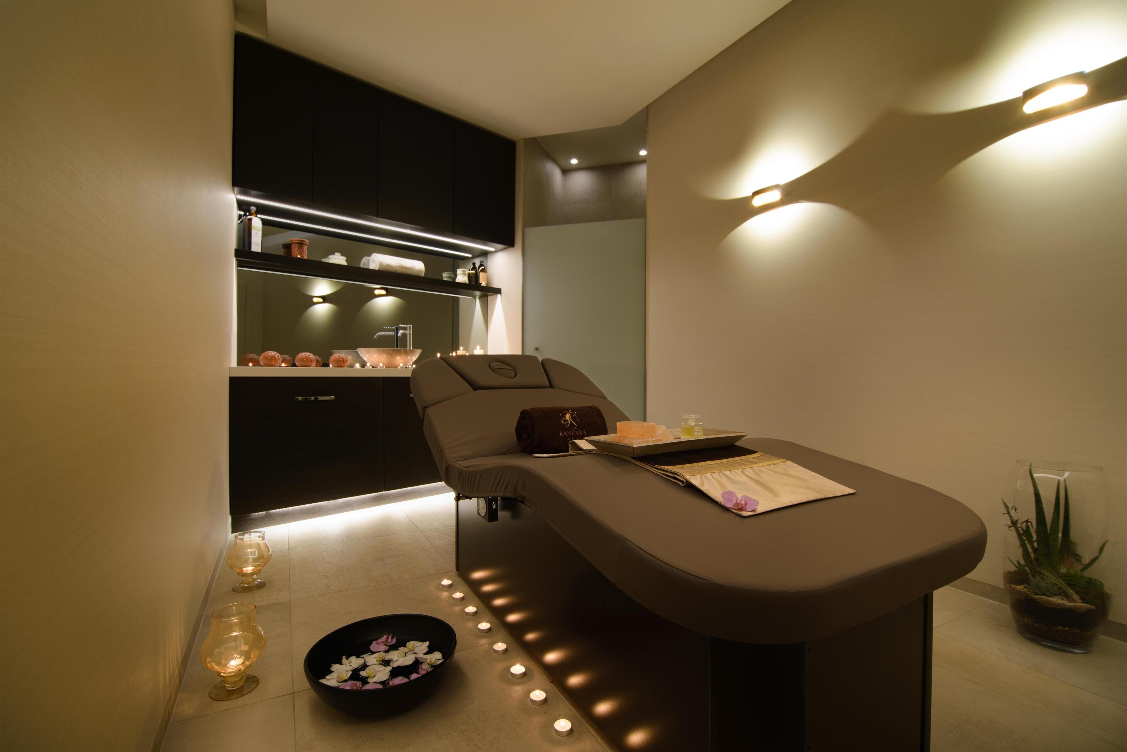 A spa room with a massage table, candles, a bowl of flowers, and a potted plant.
