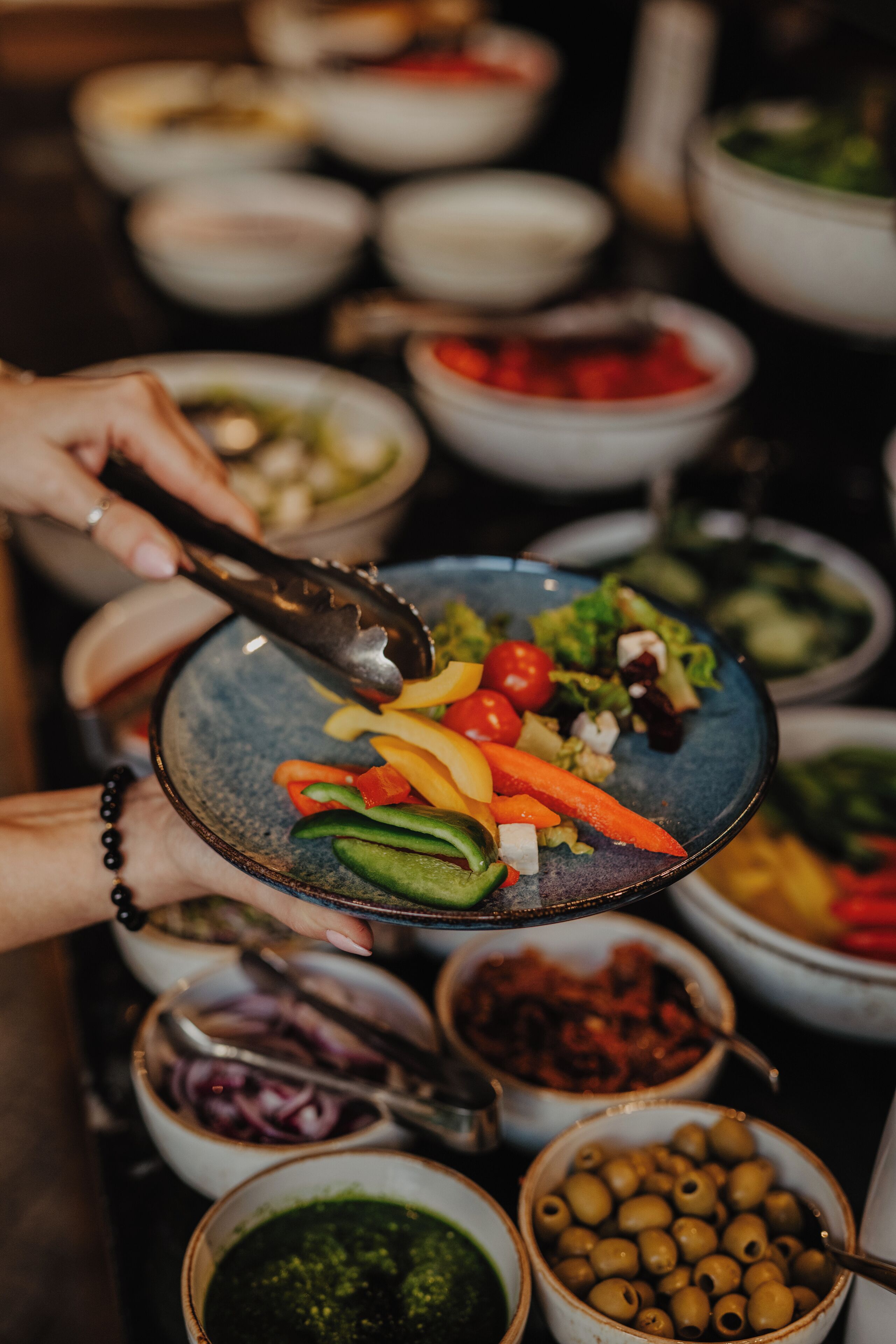 A person holding a bowl with various vegetables and olives.