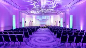 A conference room with rows of chairs facing a stage, equipped with a large screen and audio system.