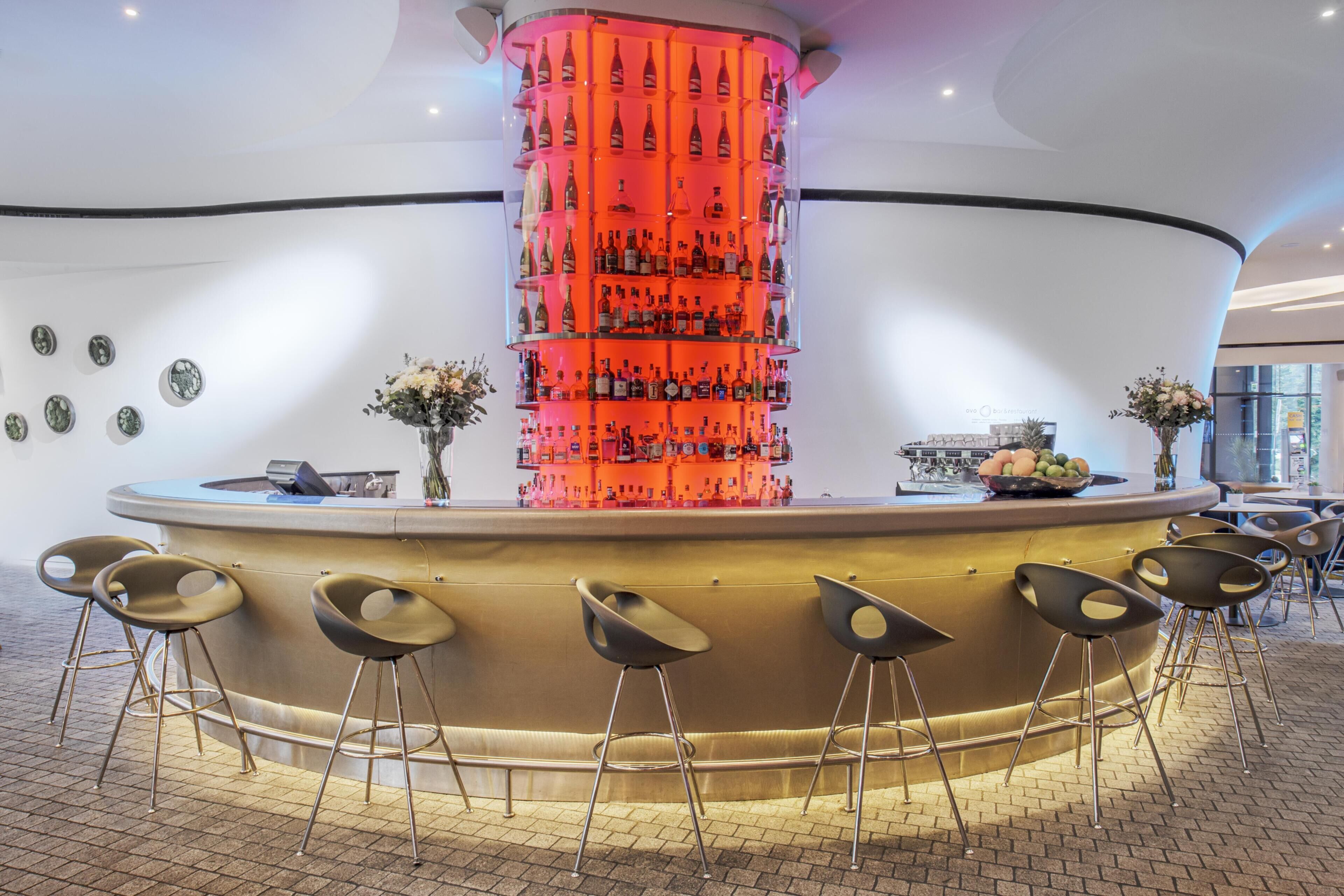 A bar area with a central column of bottles, bar stools, and a counter.