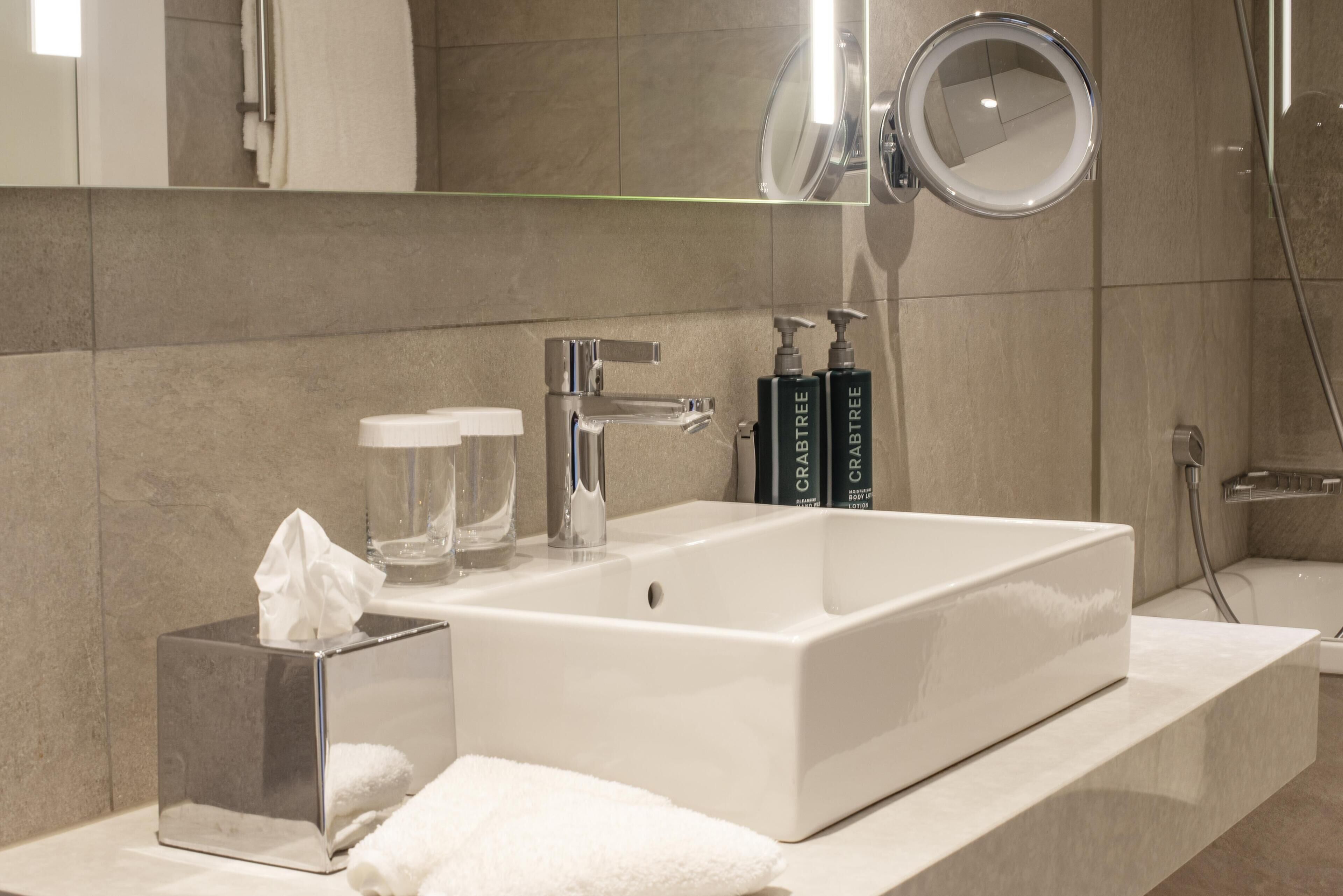 A modern bathroom with a large white sink, a mirror, and two bottles of body wash.