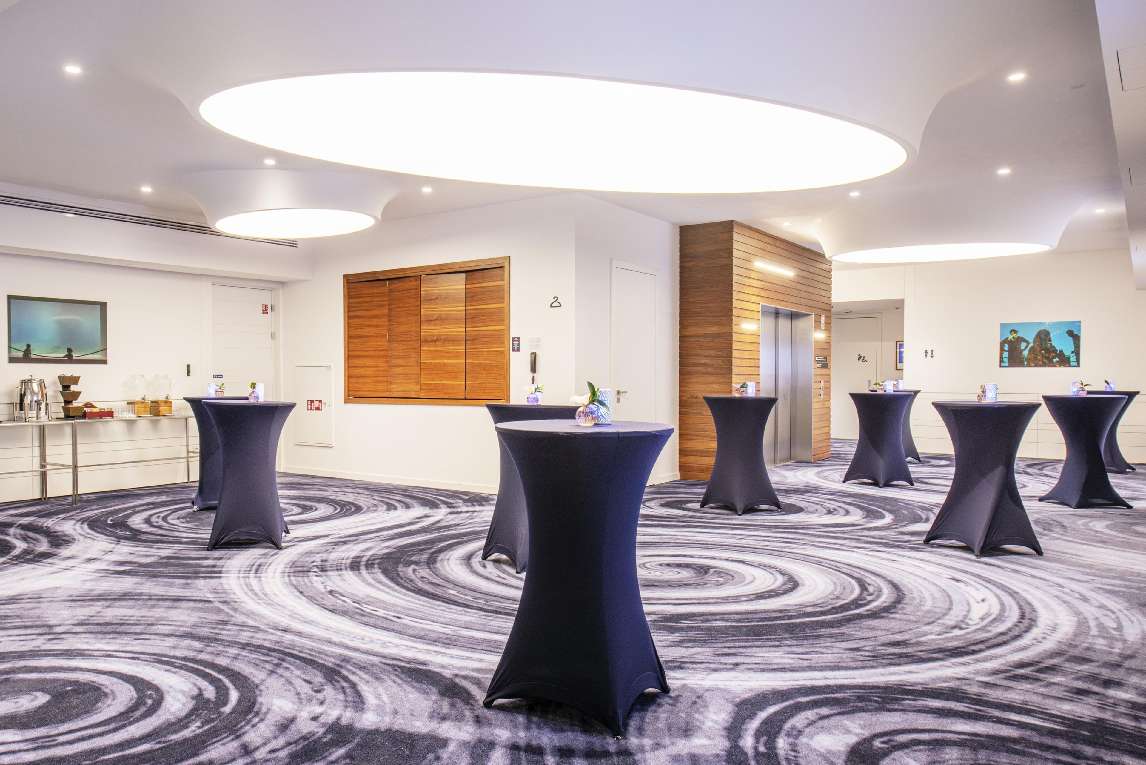 Un salón de conferencias con mesas redondas, una pared decorativa de madera y una alfombra con diseño de mármol.