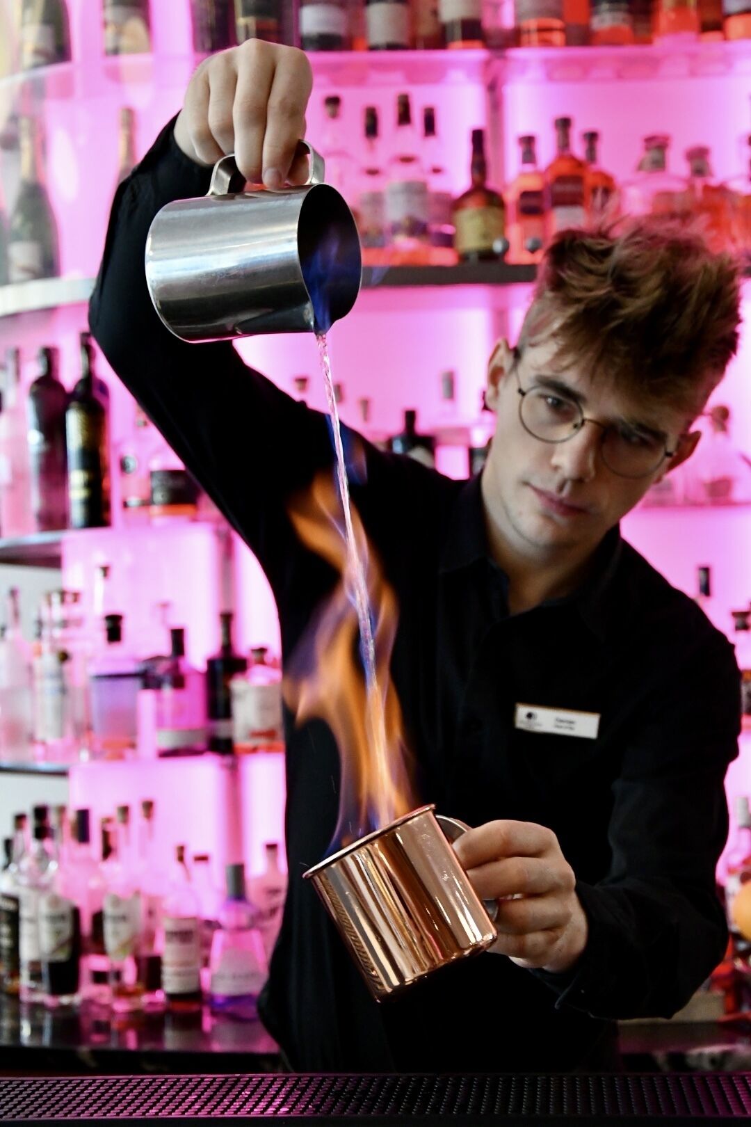 Ein Barkeeper gießt einen Drink aus einem Metallshaker in ein Kupferbecher.