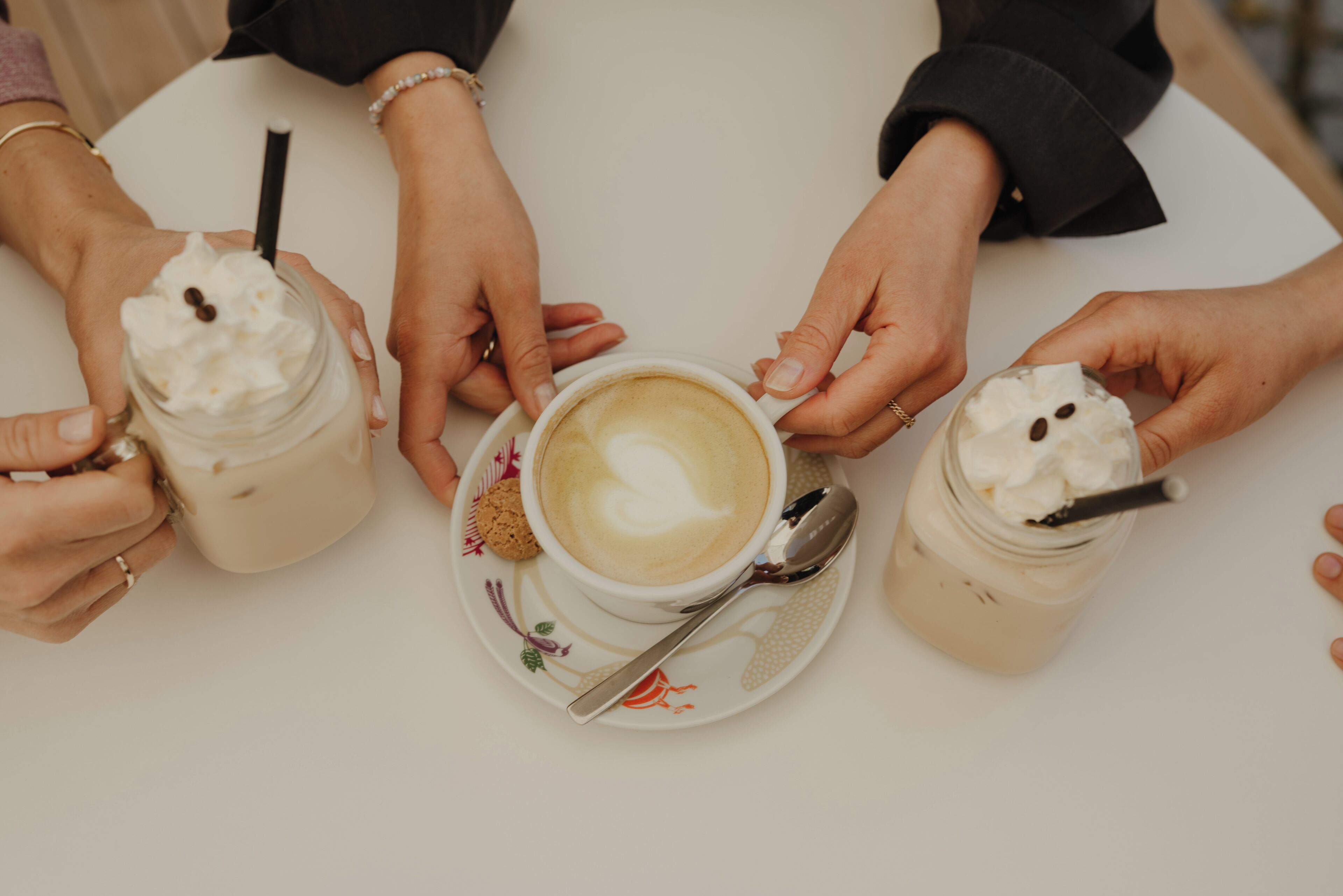 A table with three cups of coffee and two jars of whipped cream.