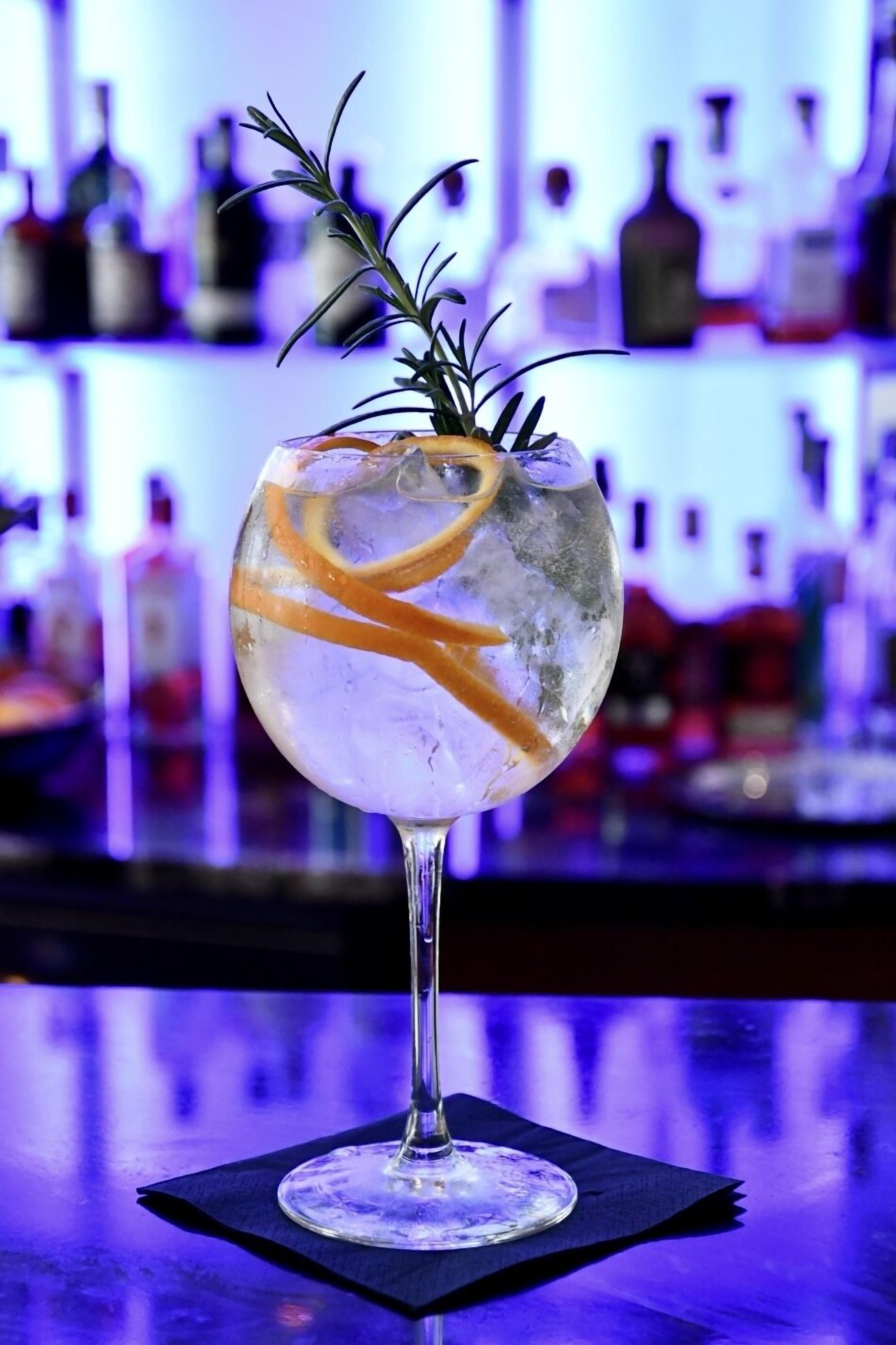 Un got de còctel amb gel, pellina d'aranja i una branca de romaní damunt un taulell de bar.