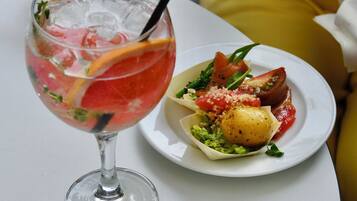 Un verre de boisson rouge avec des glaçons et une cuillère, à côté d’une assiette contenant une salade et un petit plat rond.