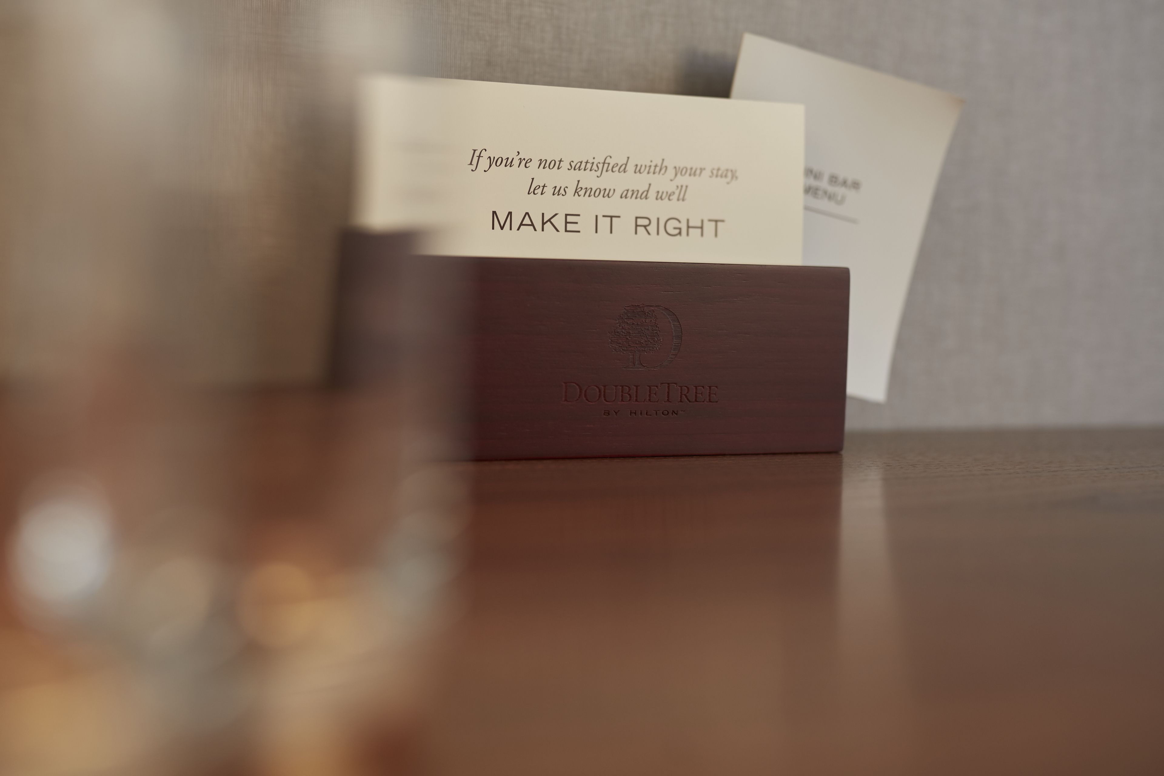 Eine Holzschatulle mit geprägtem Text 'DOUBLETREE BY HILTON' und einer Karte mit dem Text 'Falls Sie mit Ihrem Aufenthalt nicht zufrieden sind, teilen Sie es uns mit und wir werden es wieder gutmachen'.