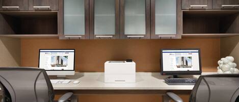Un espacio de oficina moderno con dos escritorios, cada uno con una computadora e impresora.
