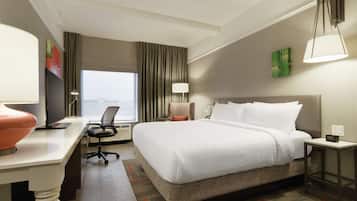 Una habitación de hotel con una cama grande, un escritorio con una computadora, una silla, una lámpara y vistas de la ciudad.