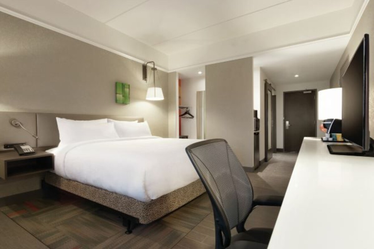 Una habitación de hotel con cama, escritorio, silla, lámpara y perchero.