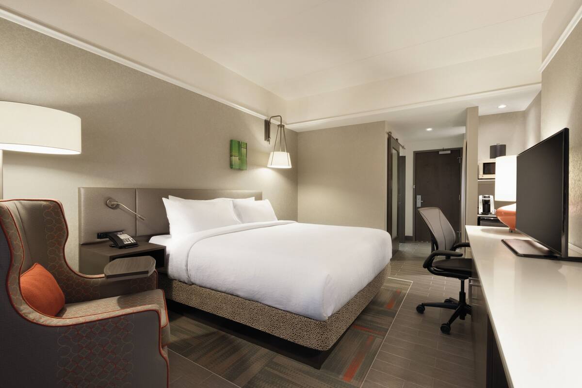 Une chambre d’hôtel avec un grand lit, un bureau avec un ordinateur, une chaise, une table de chevet et une lampe.