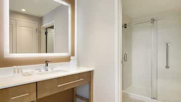 A modern bathroom with a large mirror, a white sink, and a glass-enclosed shower.