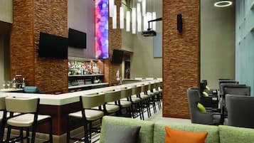 Una zona de bar con una barra larga, varios taburetes altos y una pantalla de televisión.