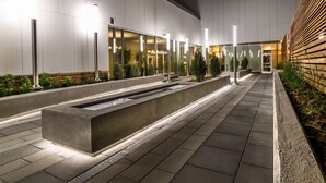 A modern building exterior with a pathway, a water feature, and greenery. - Homewood Suites by Hilton Calgary Downtown (Calgary)