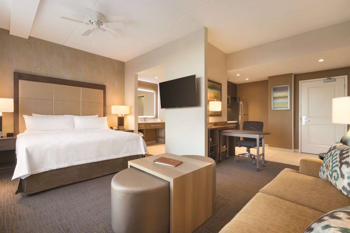 Habitación de hotel con una cama grande, un escritorio, una silla, un sofá, un televisor de pantalla plana y un ventilador de techo.