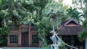 A swimming pool with a stone sculpture, a brick building, and a wooden structure in a lush garden. - Taladya Chiang Mai Homestay (Doi Saket)
