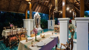An outdoor dining area with tables set for a meal, surrounded by columns and a decorative archway. - Taladya Chiang Mai Homestay (Doi Saket)