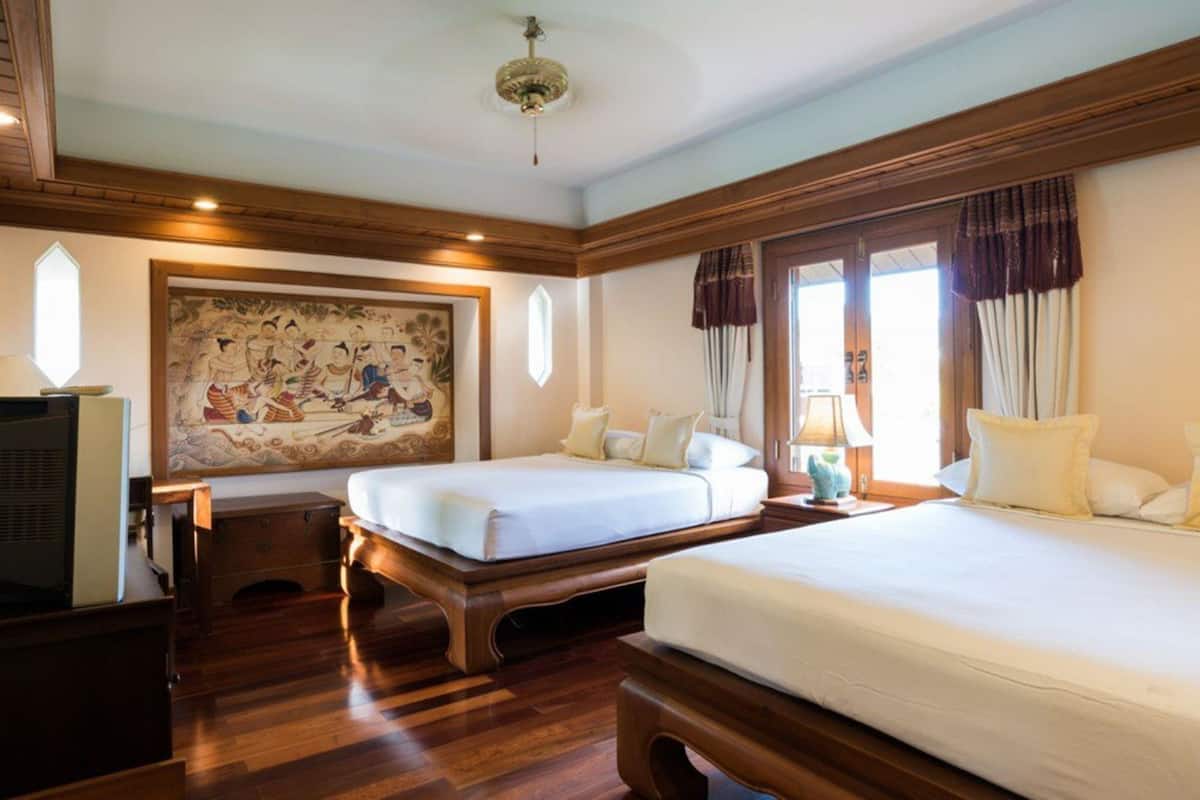 Ein Hotelzimmer mit zwei Betten, Holzboden, einem großen traditionellen Gemälde und einem Deckenventilator.