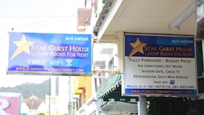 Due cartelli pubblicitari per Star Guest House: camere di lusso in affitto, con connessione WiFi gratuita, camere completamente arredate, aria condizionata, acqua calda, cassaforte in camera, TV via cavo, frigorifero e servizio di pulizia quotidiano. Sono presenti anche le informazioni di contatto.