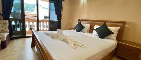 A hotel room with a large bed, a wooden headboard, a nightstand, a chair, a balcony with a view, and an air conditioning unit.