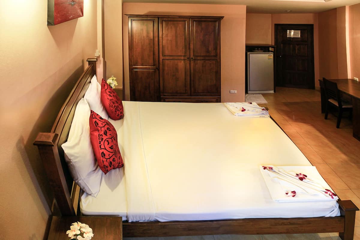 Una cama bien hecha con sábanas blancas y almohadas decorativas rojas, un cabecero de madera y un pequeño florero con flores blancas sobre una mesita de noche.
