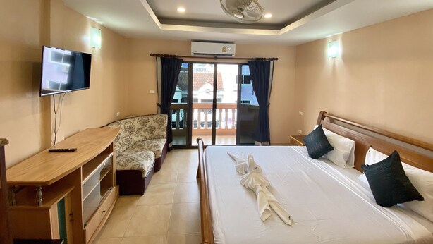 Una camera d'albergo con un letto, una TV, una scrivania, un divano e un balcone con tende.