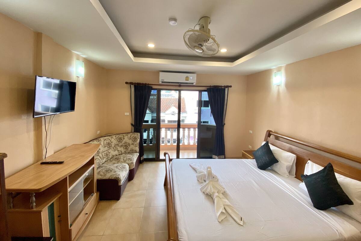 Una habitación de hotel con cama, televisión, escritorio, sofá y balcón con cortinas.