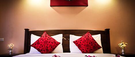 A neatly made bed with red and white pillows, a vase of flowers on the nightstand, and a wall-mounted air conditioner above.
