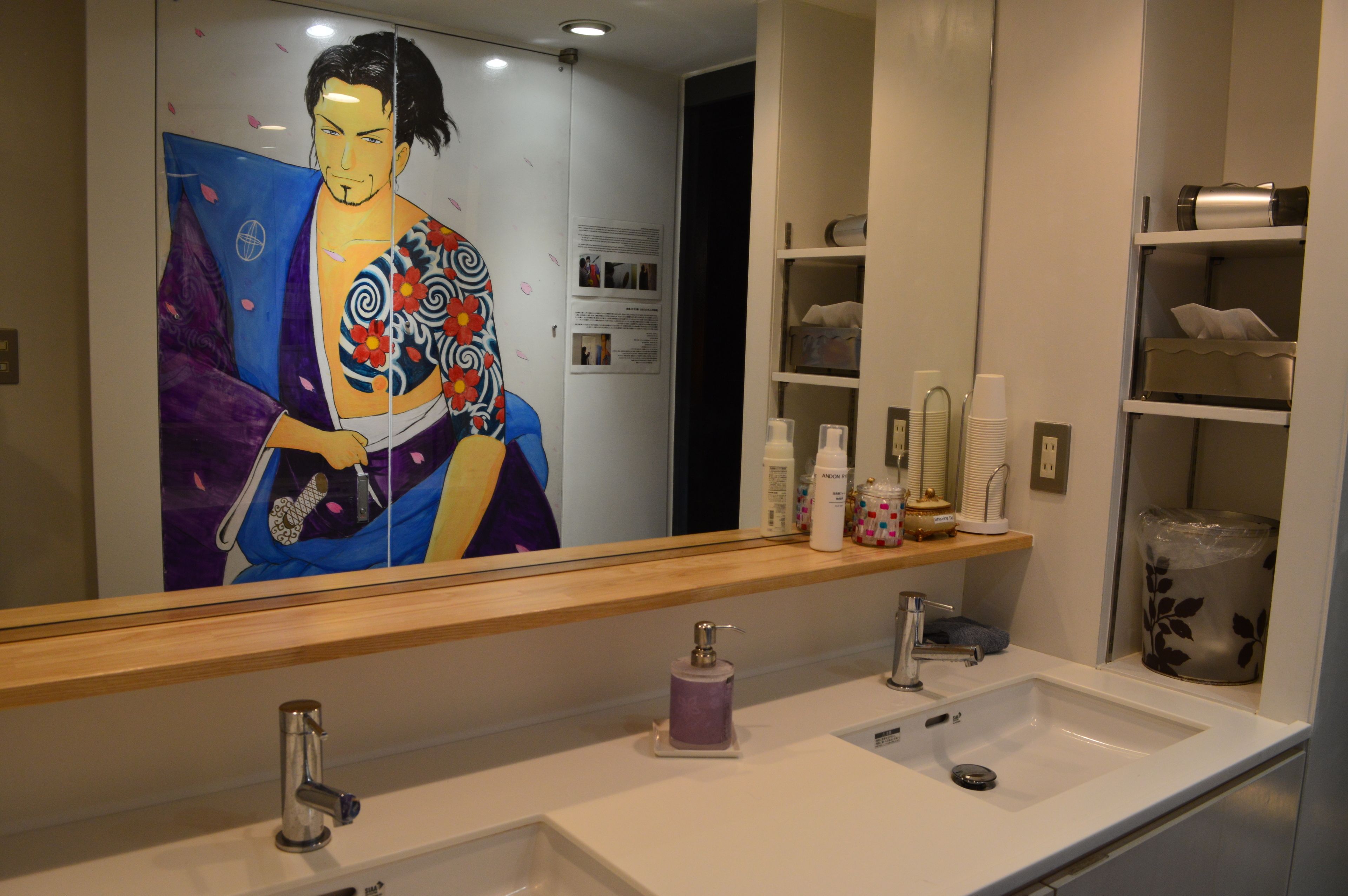 A bathroom with a large mirror, two sinks, a towel rack, and a shelf with toiletries.
