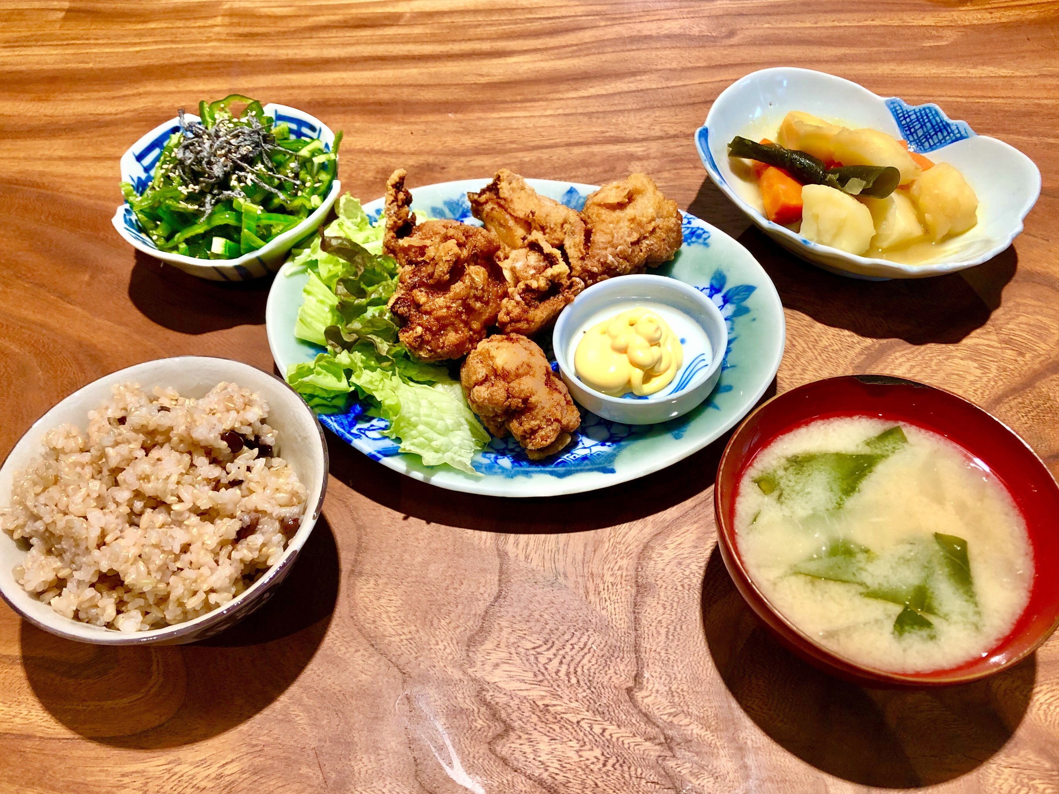 A table with various dishes including fried chicken, rice, a salad, and a bowl of soup.