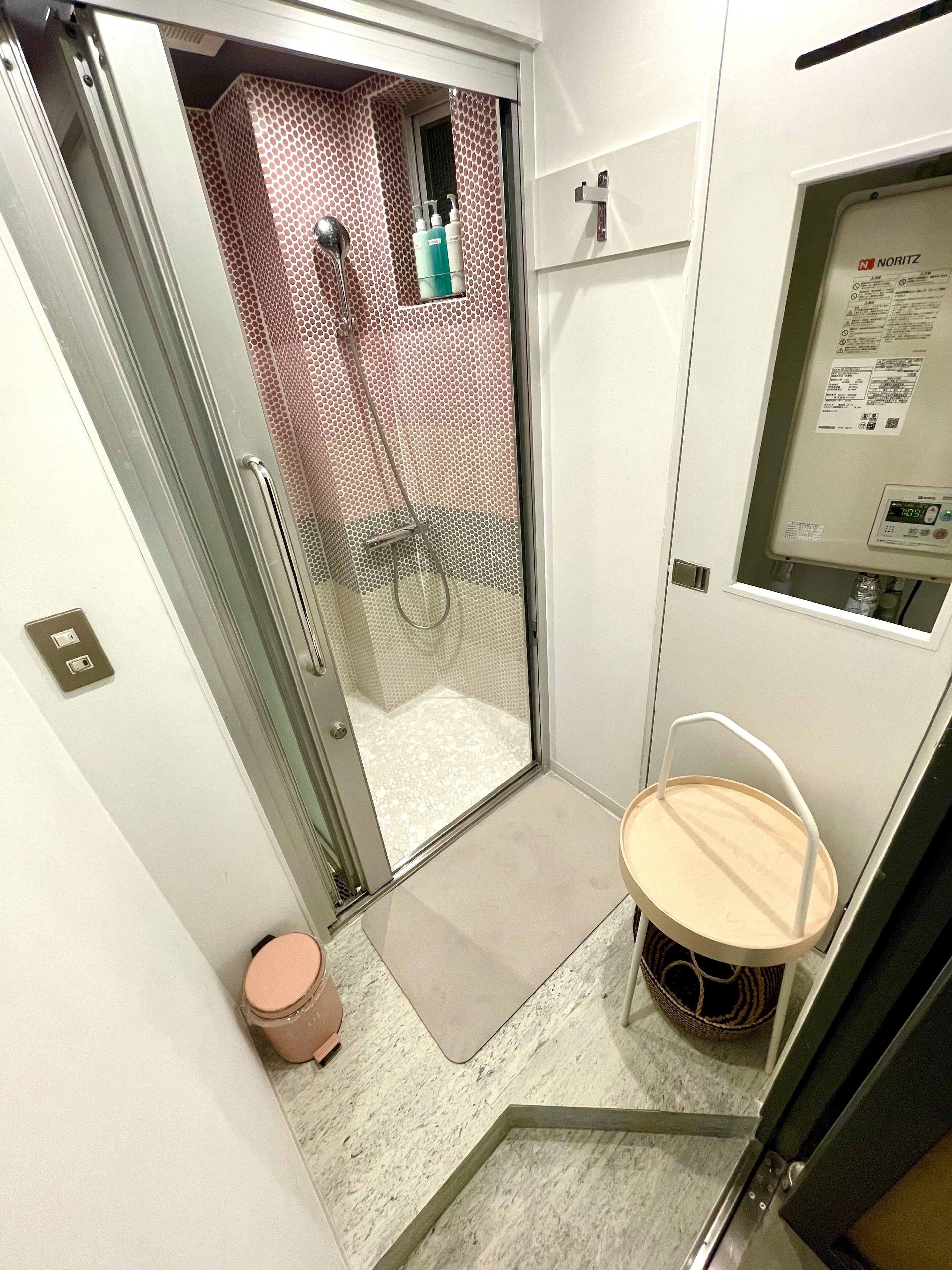 Et badeværelse med bruser, toilet og en lille træskammel.