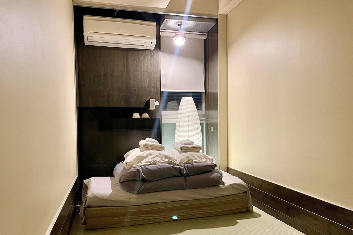 A small, narrow room with a bed, a towel rack, and an air conditioning unit.