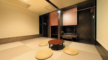 A room with tatami mats, a round wooden table, and a TV on a cabinet.