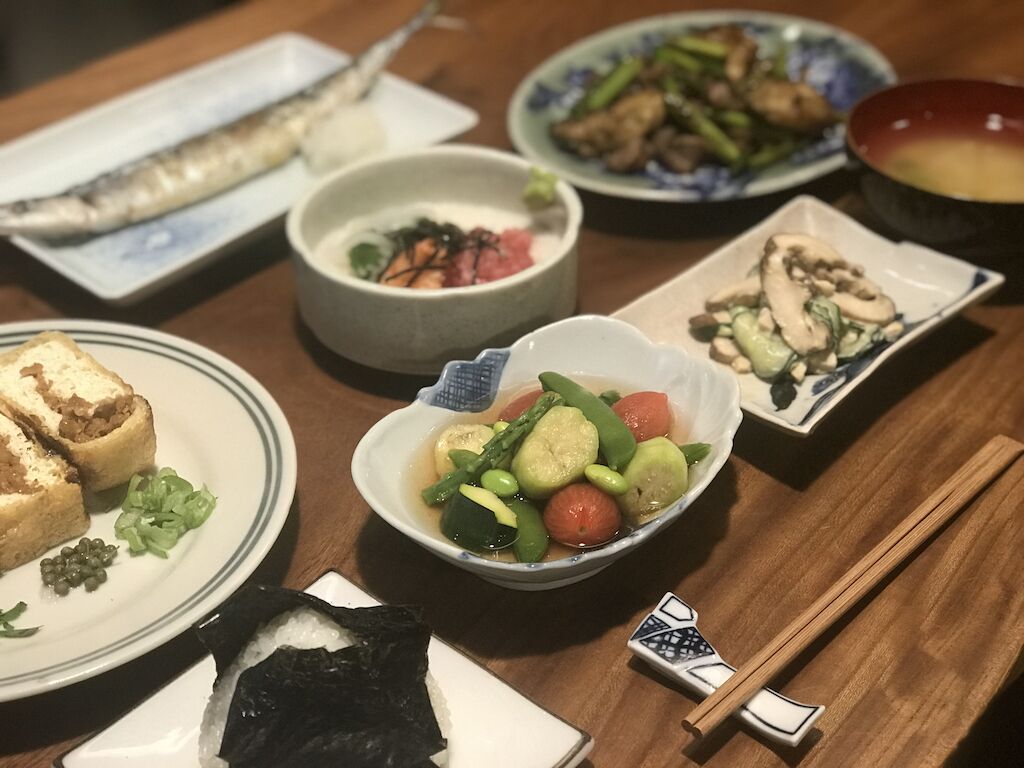 A variety of dishes on a wooden table, including fish, vegetables, and a bowl of soup.