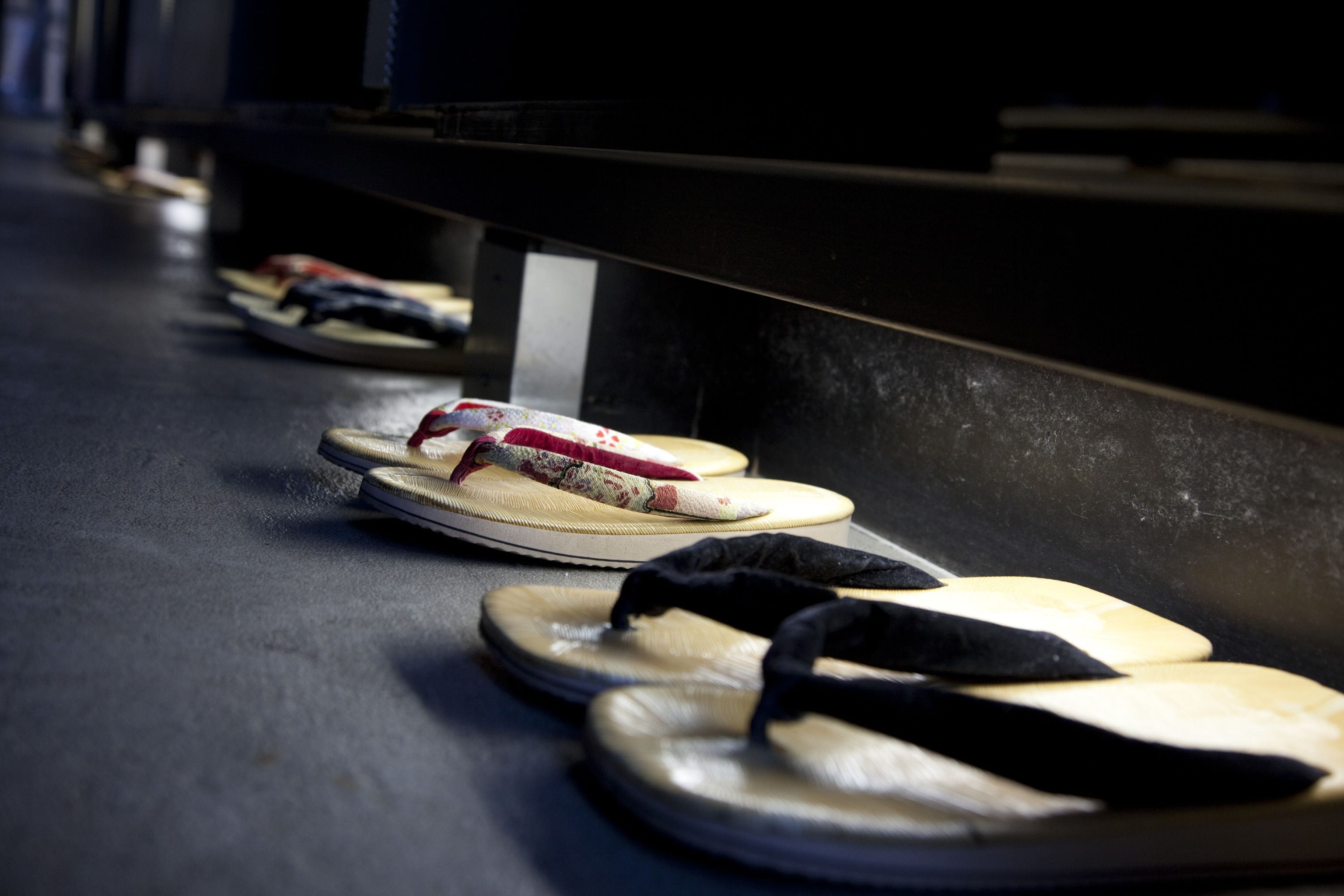 A row of flip-flops lined up on a dark surface, possibly a conveyor belt or a table.