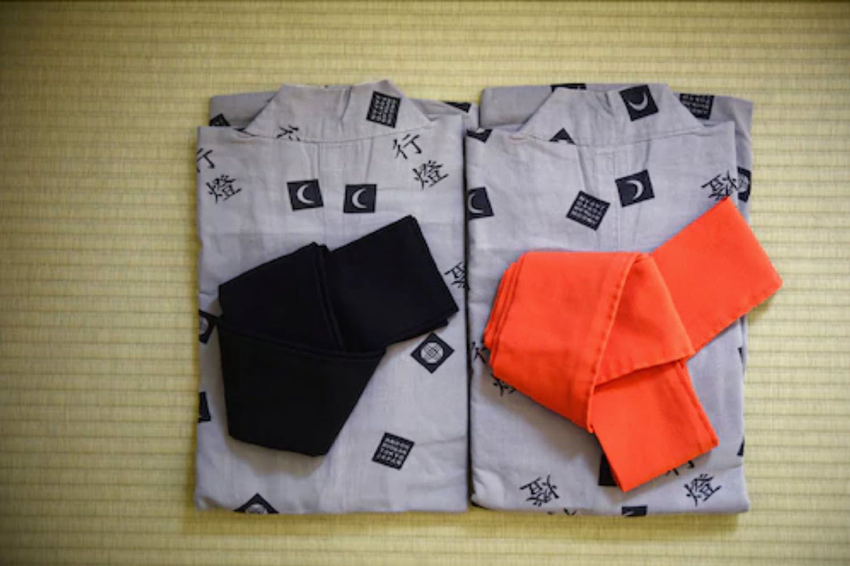 Two neatly folded garments, one black and one orange, on a patterned fabric.