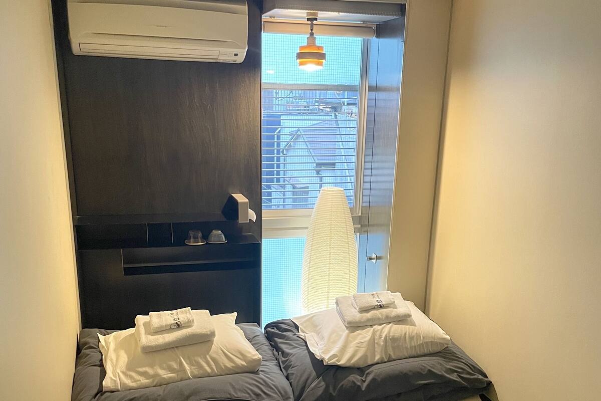 A small, compact room with a bed, a window, and a ceiling fan.