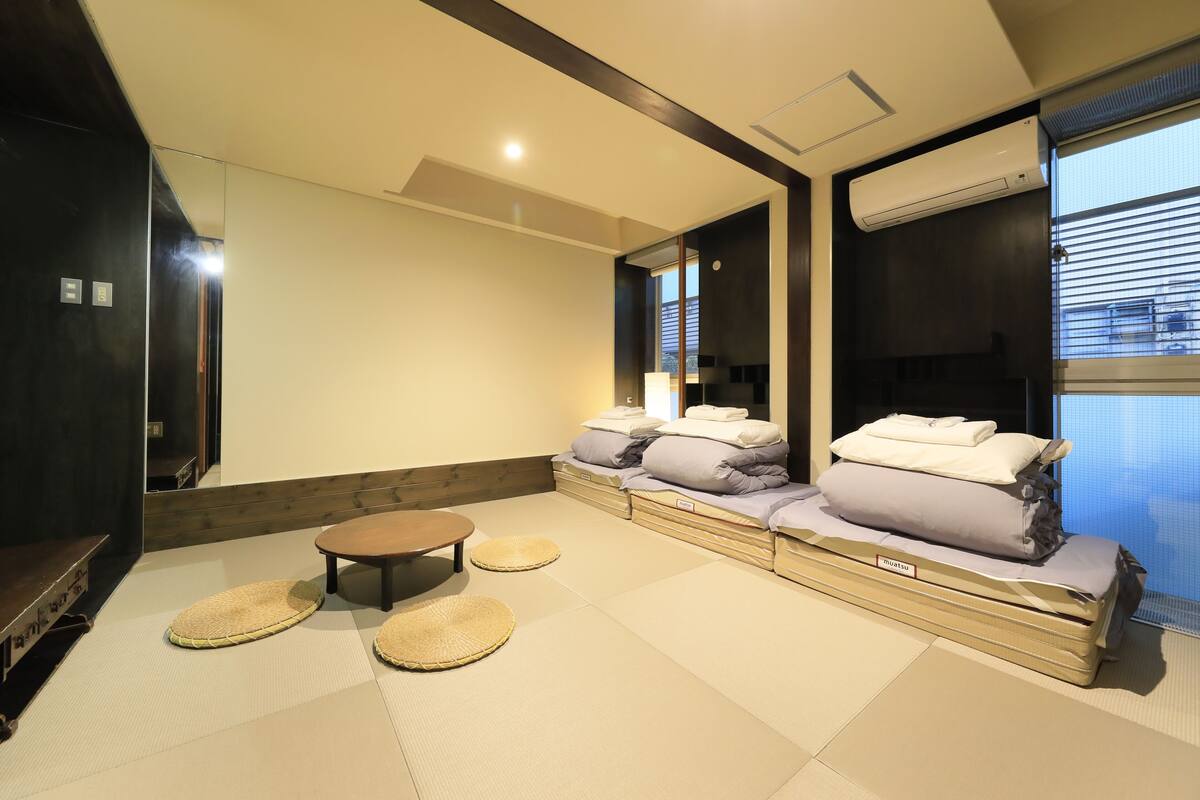A modern room with tatami mats, a low wooden table, and a futon bed with pillows.