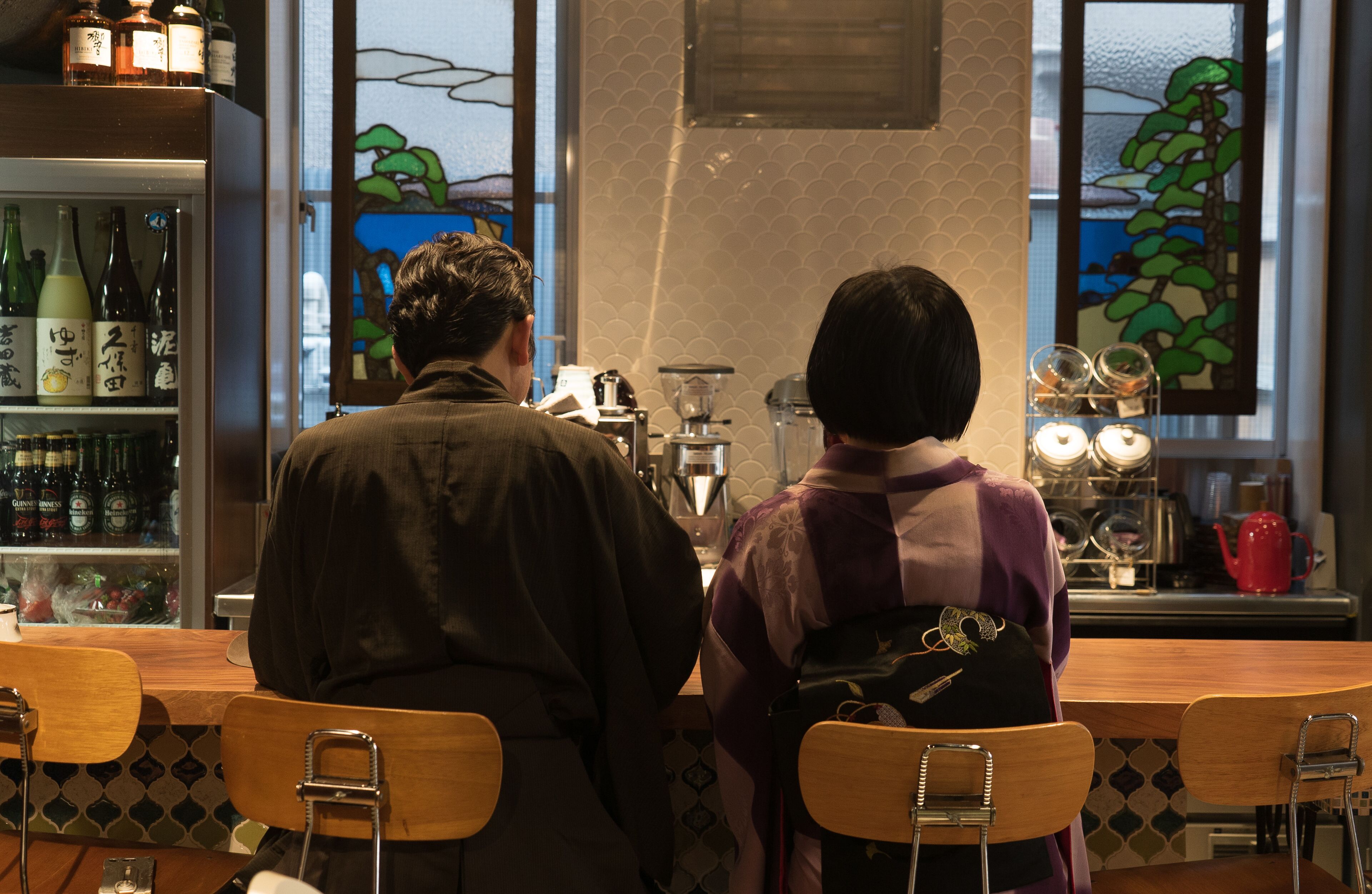 A couple seated at a wooden table in a restaurant with a bar in the background.