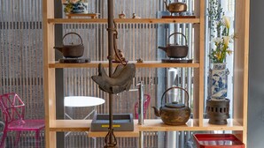 Una habitación japonesa tradicional con suelo de tatami, un estante de madera con utensilios para el té y vistas de un paisaje urbano a través de una pantalla shoji.